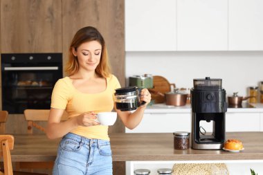 Genç bir kadın mutfakta fincana kahve dolduruyor.