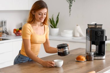 Mutfakta kahve demliği ve fincanı olan genç bir kadın.