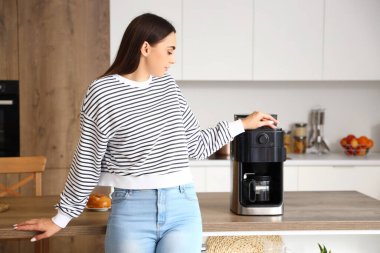 Mutfakta kahve makinesi olan genç bir kadın.