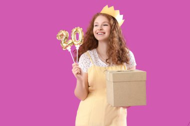 Mutlu, güzel bir kadın, doğum günü hediyesi ve mor arka planda 20 şeklinde balonlar.