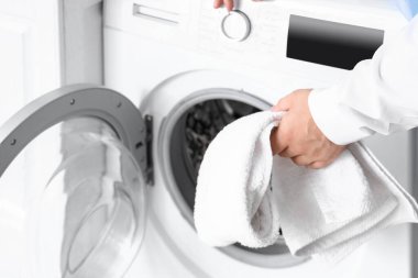 Delikanlı çamaşır makinesine çamaşır koyuyor.