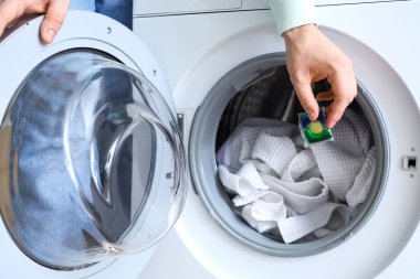 Çamaşır kapsülünü çamaşır makinesine koyan genç adam, yakın plan.