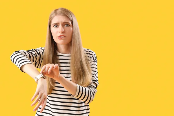 Stressed young woman with wristwatch on yellow background. Deadline concept
