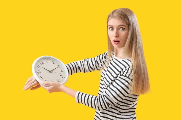 Stressed young woman with clock on yellow background. Deadline concept