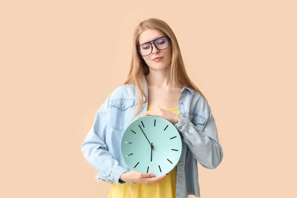 Young woman with clock on beige background. Deadline concept