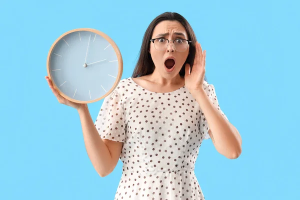 Shocked young woman with clock on blue background. Deadline concept