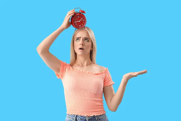 Stressed young woman with alarm clock on blue background. Deadline concept