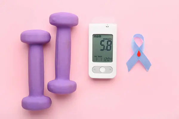 stock image Glucometer with result of sugar level measurement, dumbbells and blue ribbon on pink background. Diabetes concept