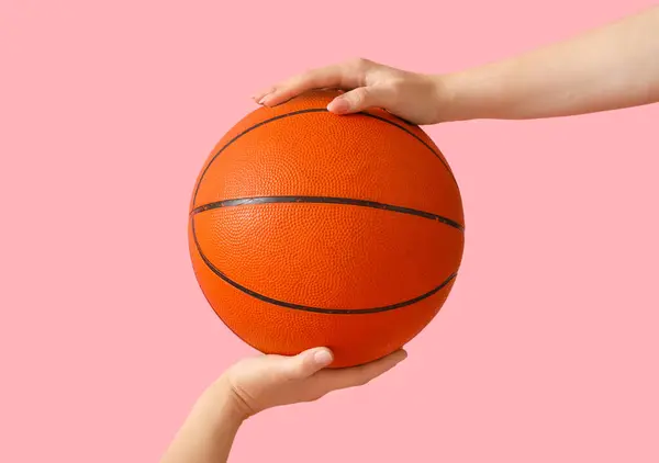 Female hand holding ball for playing basketball on pink background