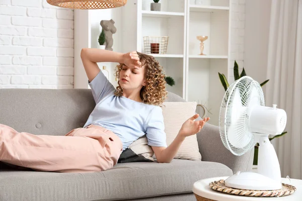 stock image Beautiful young woman with electric fan lying on sofa in living room during heatwave