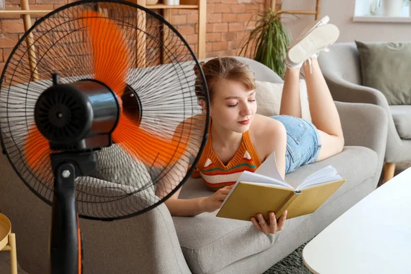 Young Woman Blowing Electric Fan Reading Book Sofa Home — Stock Photo, Image