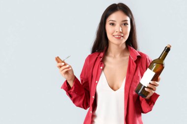 Gri arka planda şarap şişesi ve tirbuşonu olan güzel bir Asyalı kadın.