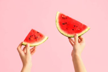 Pembe arka planda taze karpuz dilimleri olan kadın elleri.