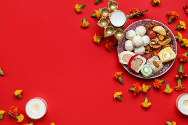 Kavurucu lambalı mumlar, kadife çiçekleri ve kırmızı arka planda bir tabak şeker. Divaly kutlaması