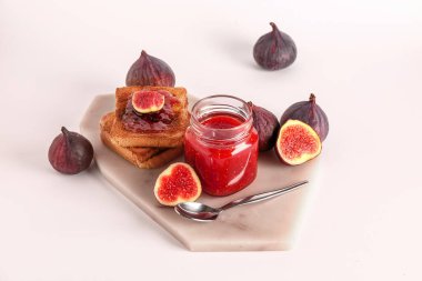 Beyaz arka planda bir kavanoz tatlı incir reçeli ve lezzetli kızarmış ekmek.