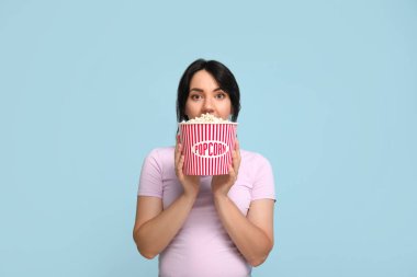 Mavi arka planda bir kova patlamış mısırla şaşırmış genç bir kadın.