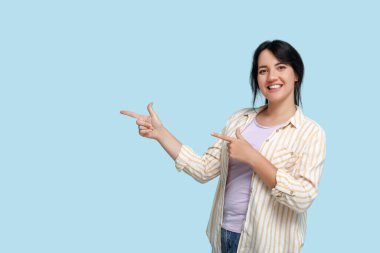 Mavi arka plandaki bir şeyi işaret eden mutlu genç esmer portresi.