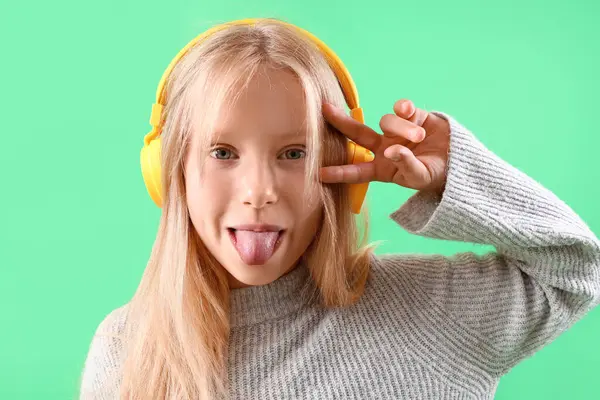 Kulaklıklı Küçük Kız Yeşil Arka Planda Zafer Jesti Sergiliyor — Stok fotoğraf