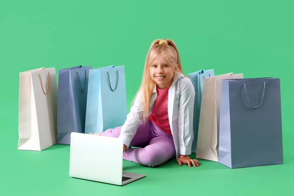 Little girl with laptop and shopping bags sitting on green background