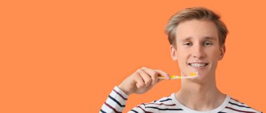 Diş telleri ve turuncu arka planda diş fırçası olan genç bir adam.