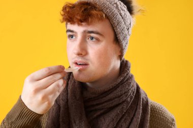 Öksürük şurubu alan genç adam sarı arka planda, yakın plan