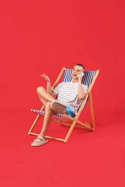 Güvertede oturan ve kırmızı arka planda cep telefonuyla konuşan mutlu genç adam.