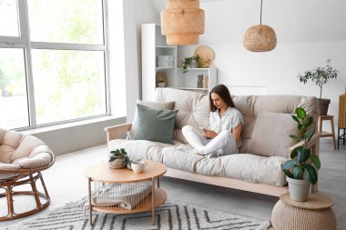 Oturma odasındaki koltukta cep telefonu kullanan genç bir kadın.