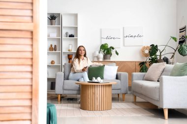 Oturma odasındaki kanepede televizyon izleyen genç bir kadın.