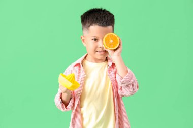 Meyve sıkacağı ve yeşil arka planda taze portakal dilimi olan küçük Asyalı çocuk.