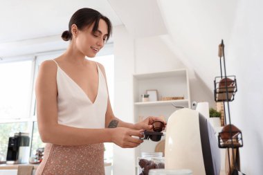 Mutfakta kahve makinesi kullanan güzel genç bir kadın.