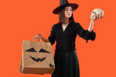 Cadılar Bayramı için cadılar bayramı için giyinmiş genç bir kadın hediye paketleri ve kafatası ile turuncu arka planda