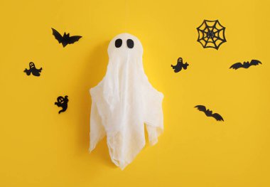 Sarı duvarda hayalet olan kağıt cadılar bayramı dekoru.
