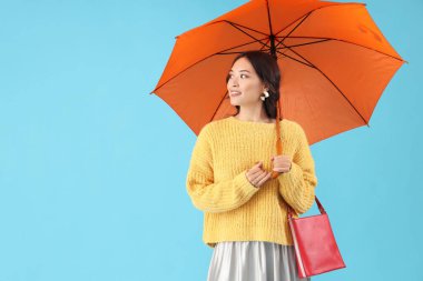 Sonbahar elbiseli, mavi arka planda şemsiyesi olan zarif Asyalı bir kadın.