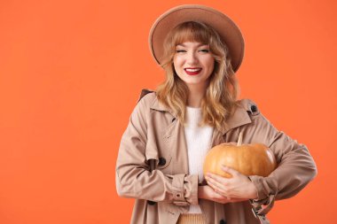 Güz kıyafetleri içinde, turuncu arka planda balkabağı olan şık genç bir kadın.