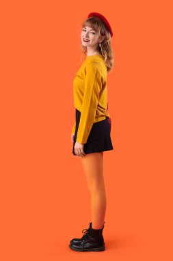 Turuncu arka planda sonbahar kıyafetleri içinde şık bir genç kadın.