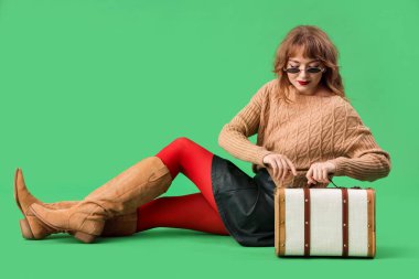 Yeşil arka planda oturan sonbahar elbiseli şık genç kadın.