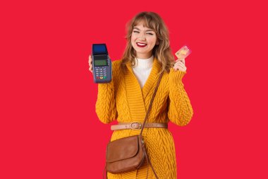 Kırmızı arka planda kredi kartı ve ödeme terminali olan şık genç bir kadın.