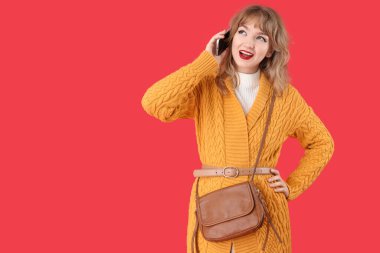 Kırmızı arka planda çantalı, güz elbiseli şık genç bir kadın.