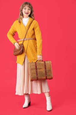 Kırmızı arka planda çantalı, güz elbiseli şık genç bir kadın.