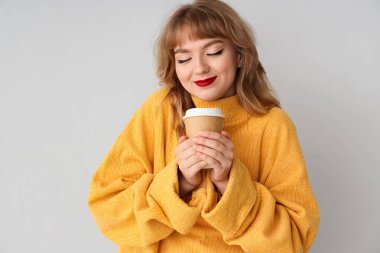 Hafif arka planda kahve fincanı olan kazaklı genç bir kadın.