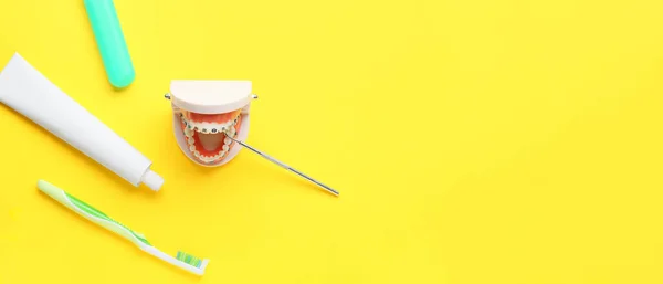 Model of jaw with dental braces, dentist\'s tool, tooth brush and paste on yellow background with space for text
