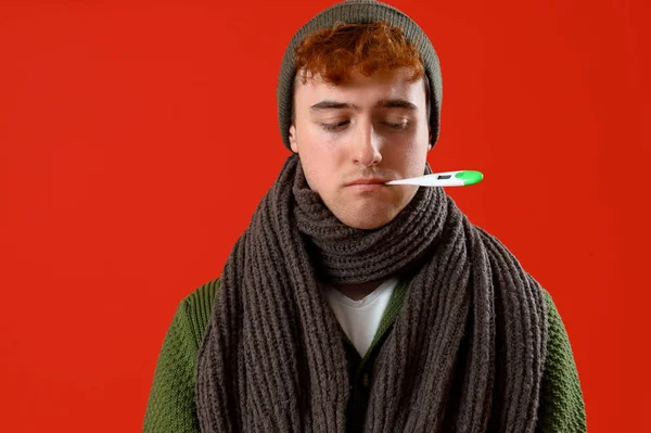 Kırmızı Arka Planda Termometreyle Sıcaklık Ölçen Hasta Genç Bir Adam — Stok fotoğraf