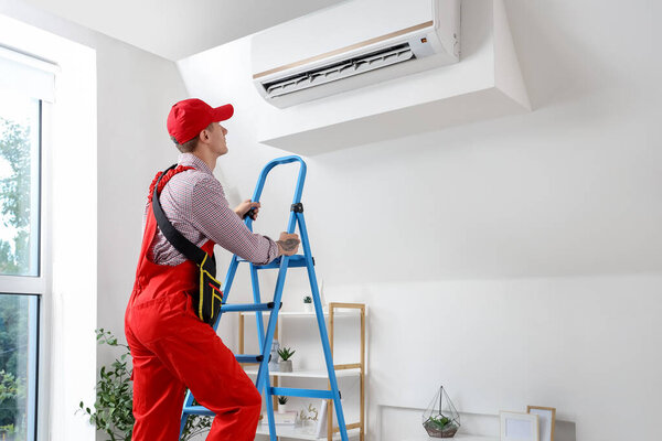 Male technician fixing air conditioner in room