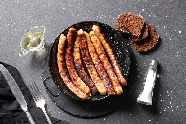 Kızartma tavası ızgara sosis ve siyah arka planda ekmek.