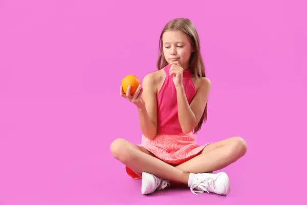 Thoughtful Little Girl Fresh Orange Sitting Purple Background — Stock Photo, Image