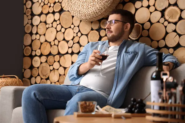 Genç sommelier bir kadeh şarapla kanepede dinleniyor.