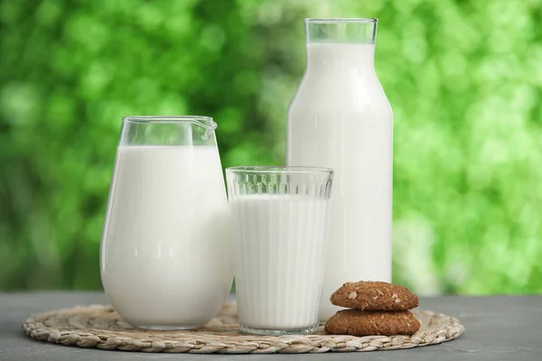 Glass and jug of fresh milk with sweet cookies on grey table outdoors