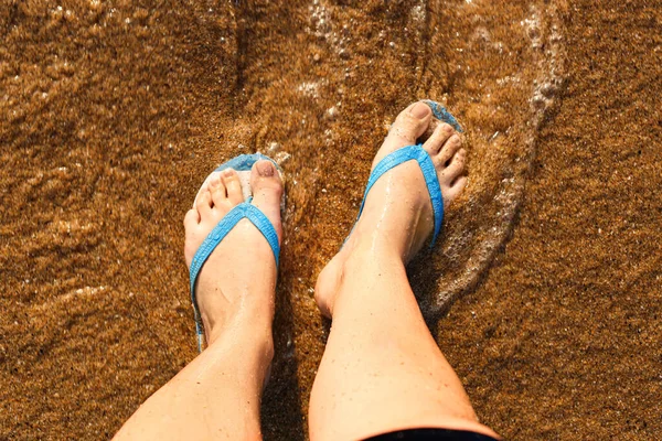 Woman in stylish flips flops on sand at resort