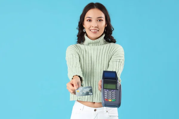 Young Asian woman with payment terminal and credit card on blue background