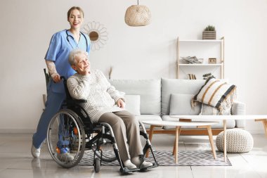 Evde tekerlekli sandalyede yaşlı bir kadınla genç bir bakıcı.